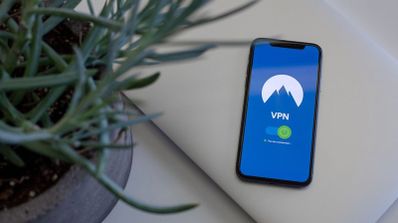 Teléfono móvil mostrando una aplicación de VPN activada junto a una planta y un portátil.