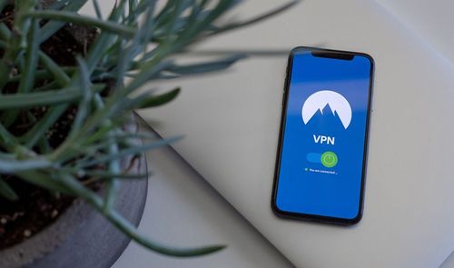 Teléfono móvil mostrando una aplicación de VPN activada junto a una planta y un portátil.
